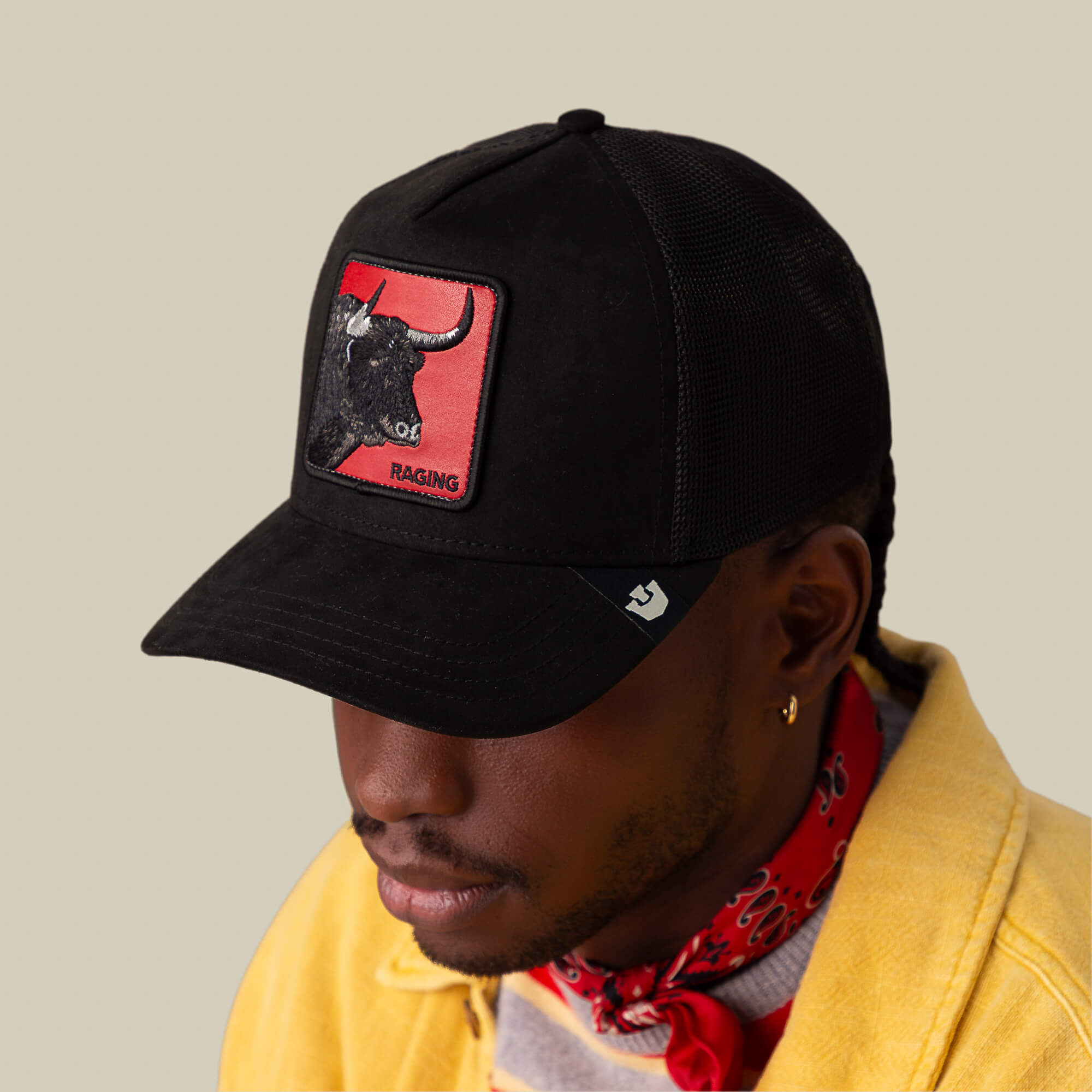 A person wearing the Goorin Bros. Toro Rosso black cap with a bull patch, paired with a yellow jacket and a red bandana, stands out with force and presence against a neutral background.