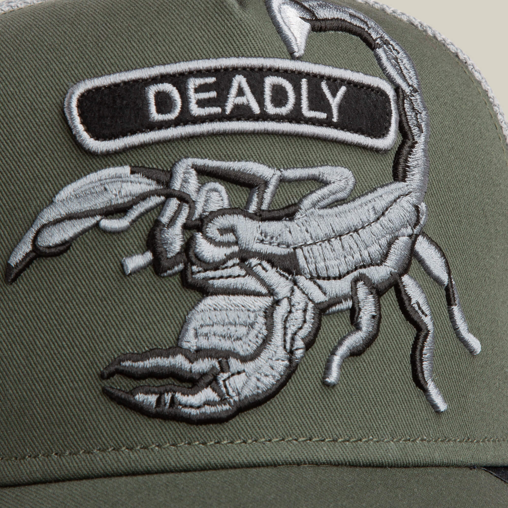 A close-up of the Goorin Bros. Classic Rocker - Deadly hat in military green, showcasing its scorpion patch and grey mesh detailing in the background.
