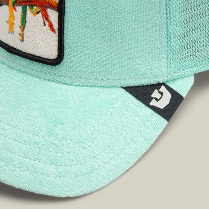 Close-up of the Terry Cloth Iguana cap by Goorin Bros.—a light teal, breathable hat with a mesh back, fabric patch featuring a colorful design, and a small white geometric logo on the brim.