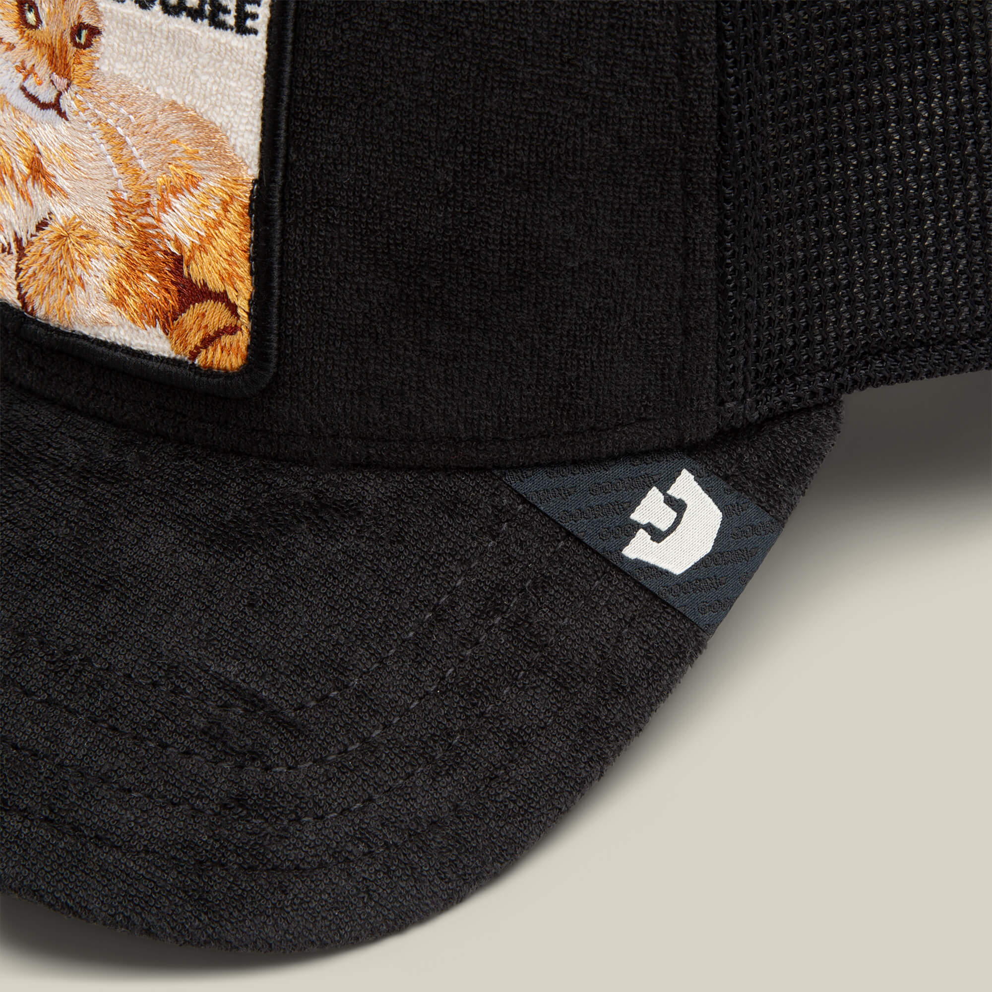 Close-up of the Goorin Bros. "Terry Cloth Cat" cap, crafted from plush black terry cloth with an embroidered orange and white cat patch and a subtle white logo on the brim, offering luxury loungewear softness.