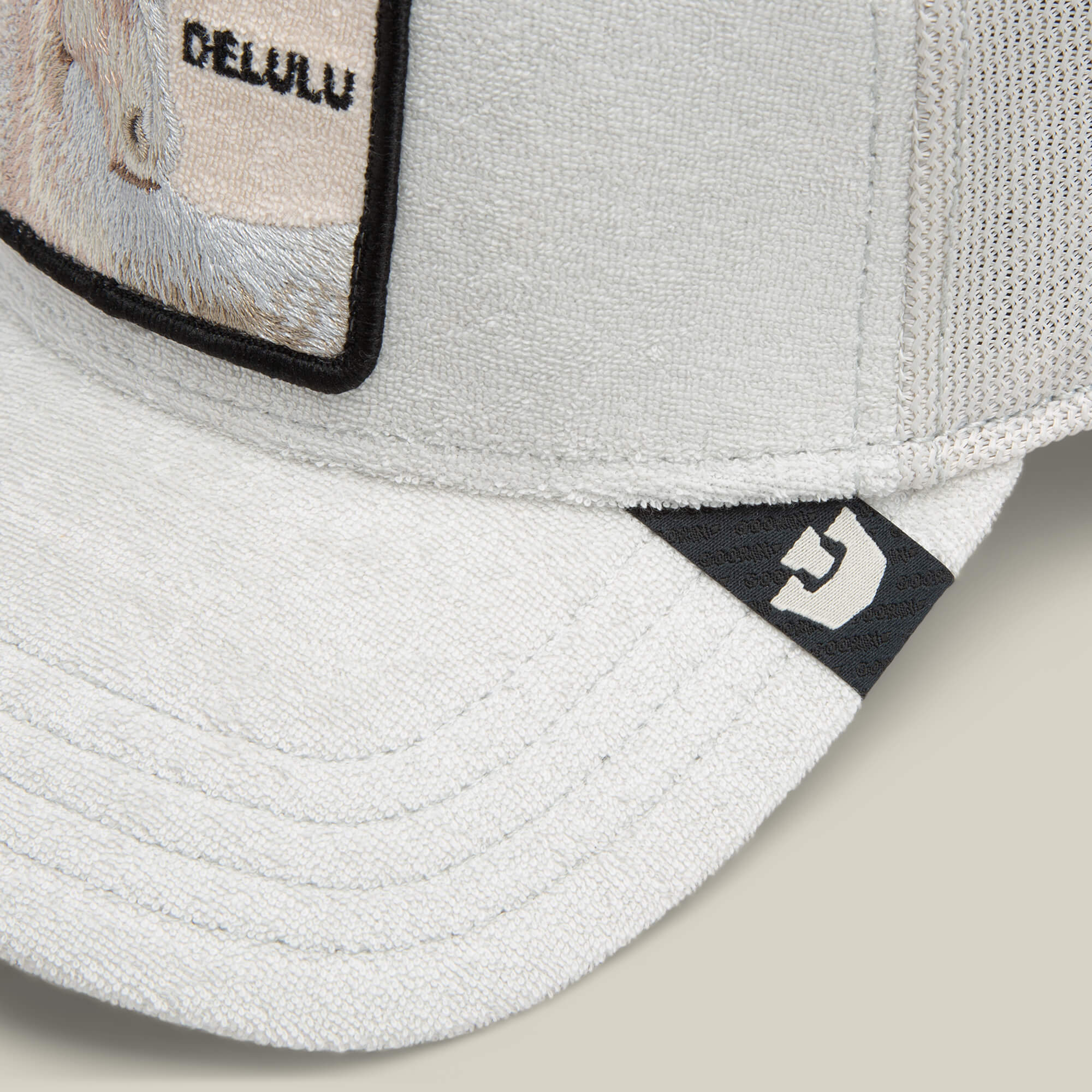 Close-up of the Goorin Bros. Terry Cloth Unicorn cap in light gray, made from soft fabric, with a rectangular patch reading DELULU and a small black logo tag on the brim.
