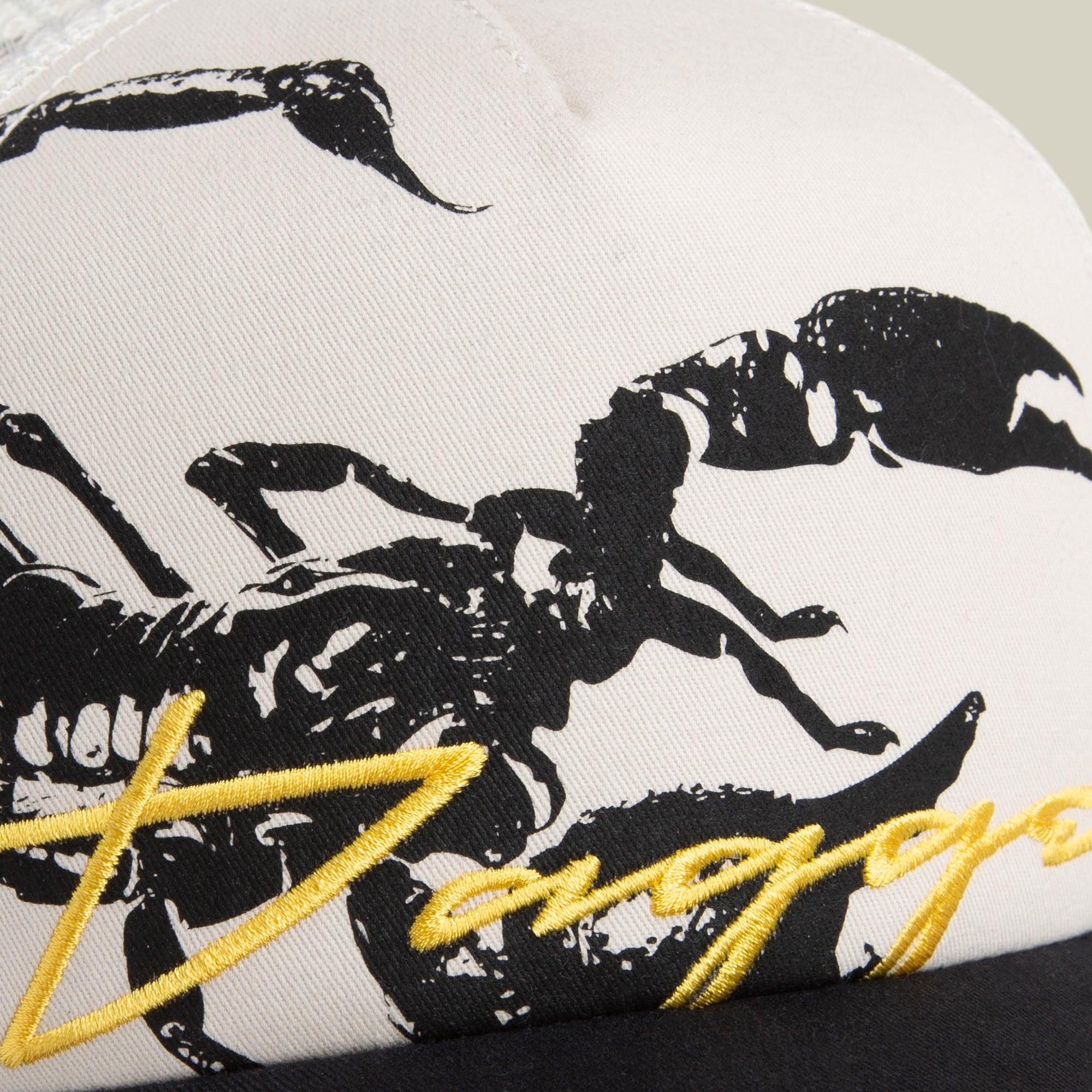 Close-up of the Goorin Bros. "Outside the Lines Scorpion" cap—cream and black with a mesh back, black scorpion print, and yellow embroidered text—shown on a light fabric background.