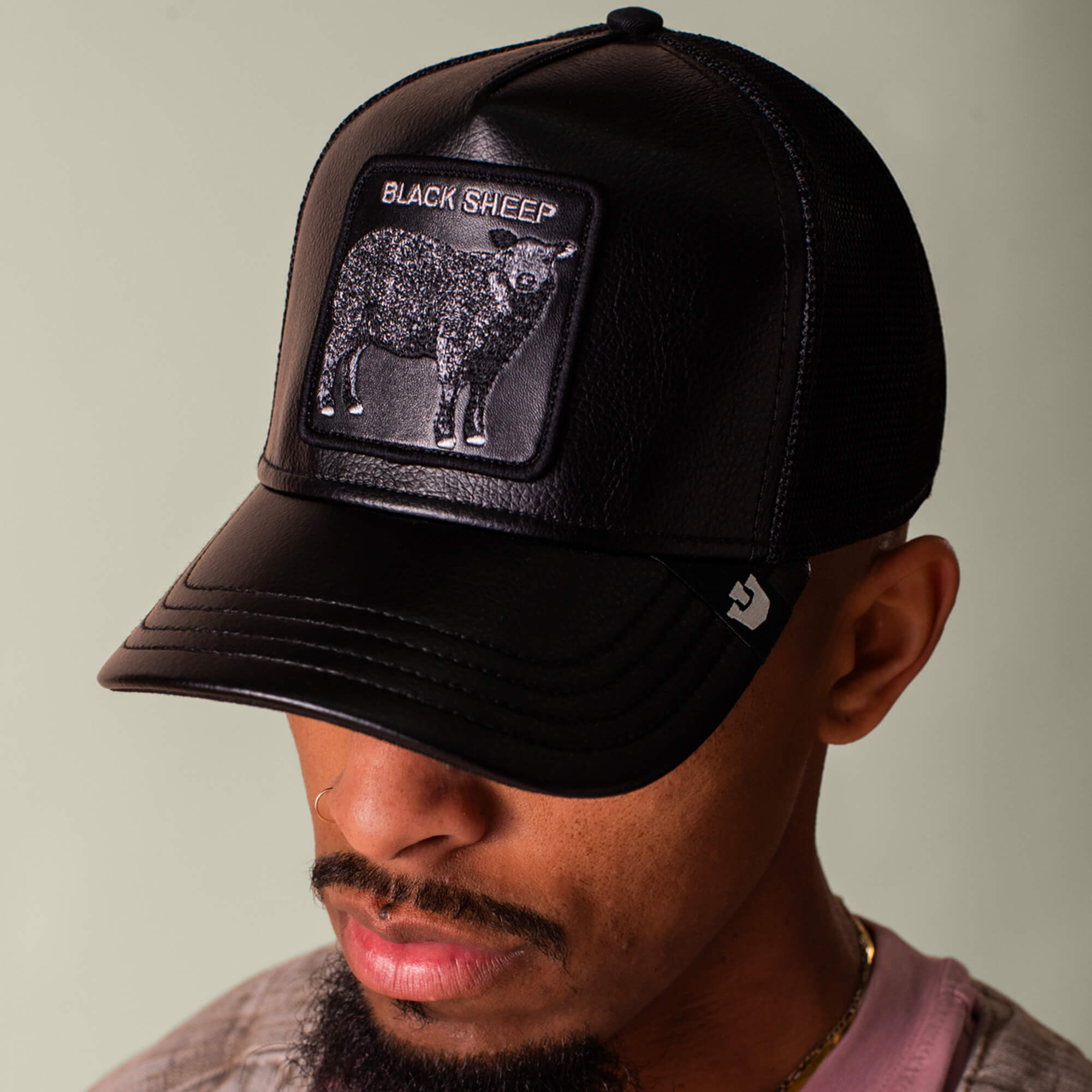 Man wearing the Goorin Bros. "Faux Leather Sheep" black mesh baseball cap, featuring a faux leather black sheep patch and image; head slightly tilted down.