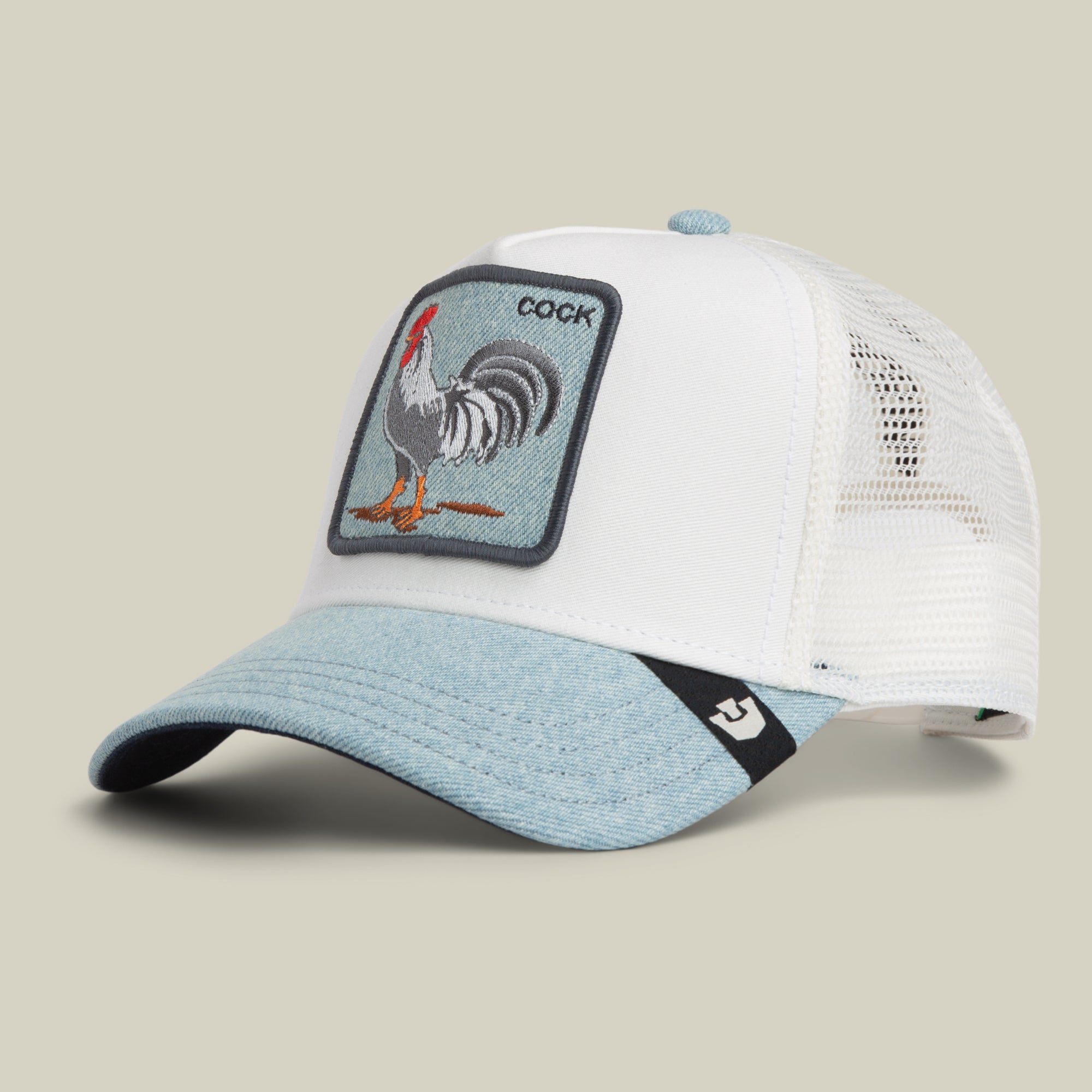 The Goorin Bros. Denim Rooster is a white and light blue denim trucker hat featuring a rooster patch with the word “COCK.” This trucker hat has a mesh back and a curved brim.