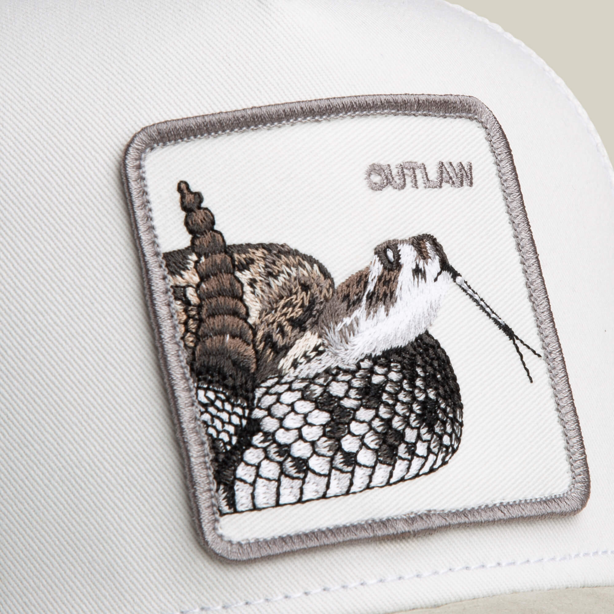 Close-up of the Goorin Bros. Suede Rattlesnake hat, featuring a white cap, suede brim, embroidered rattlesnake patch, and "OUTLAW" stitched in the upper right corner.