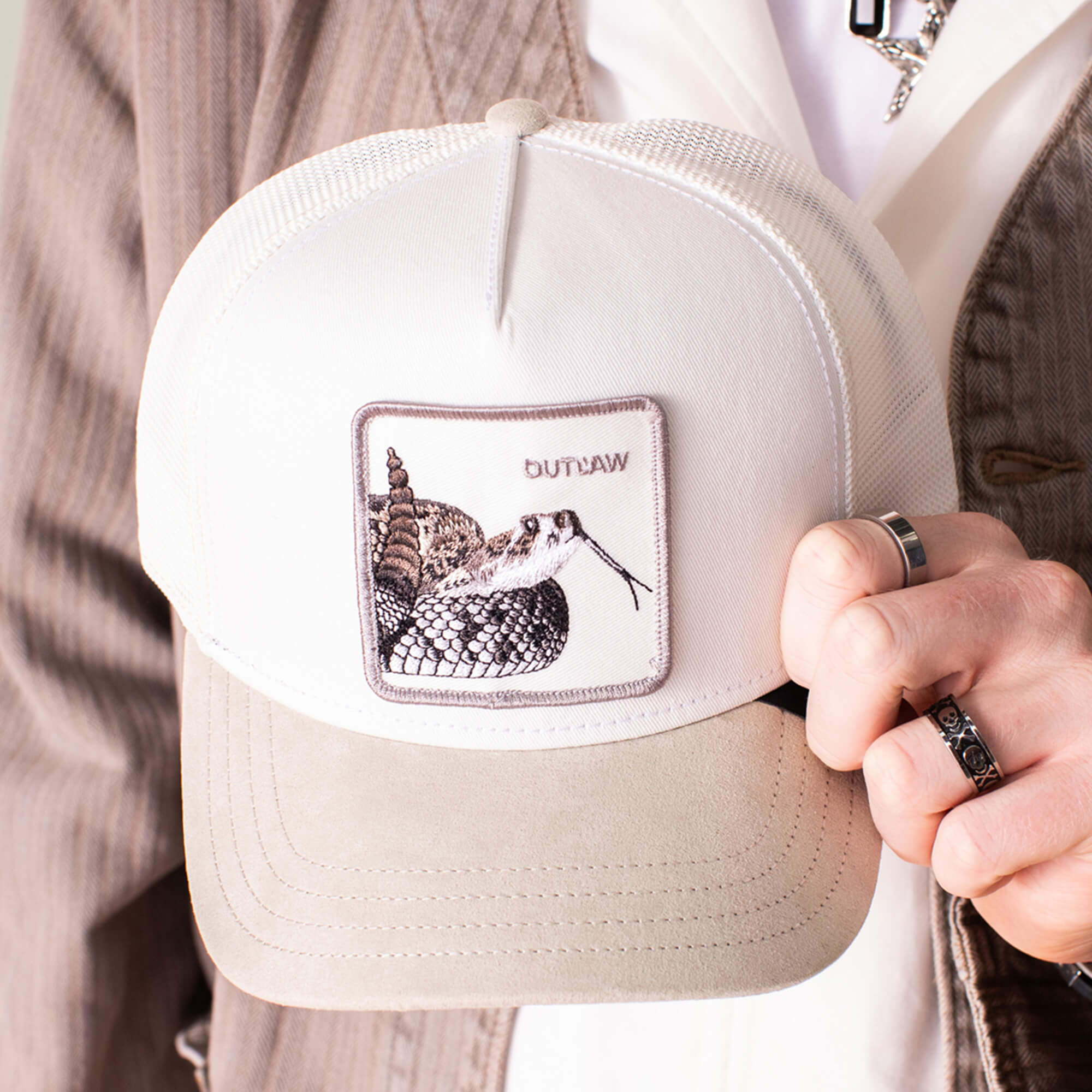 A person holding the Goorin Bros. Suede Rattlesnake hat, featuring a white and beige design, suede brim, and a rattlesnake patch with "OUTLAW".