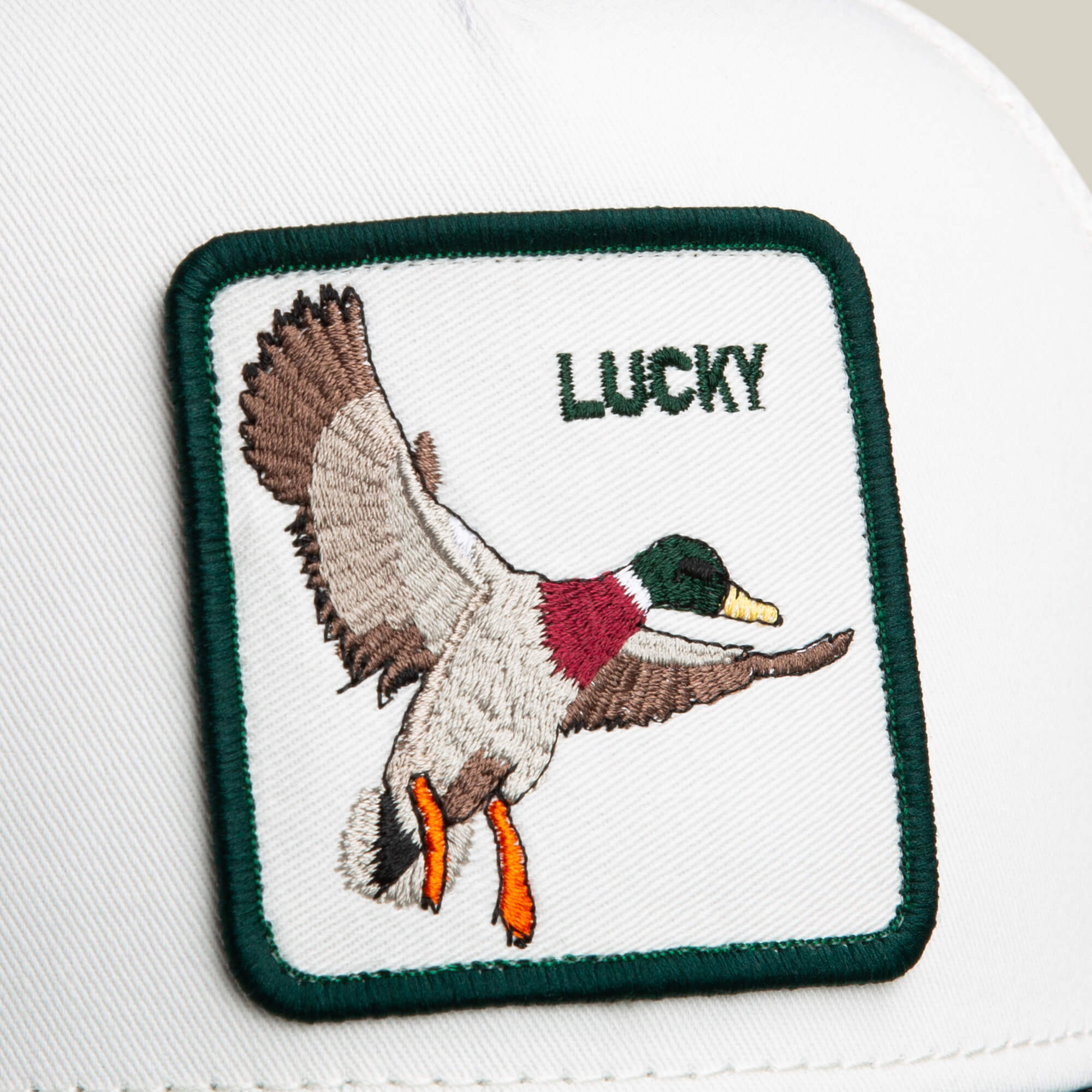The Goorin Bros. Suede Duck is a white and green hat with a square patch featuring an embroidered flying duck and "LUCKY" in green text.