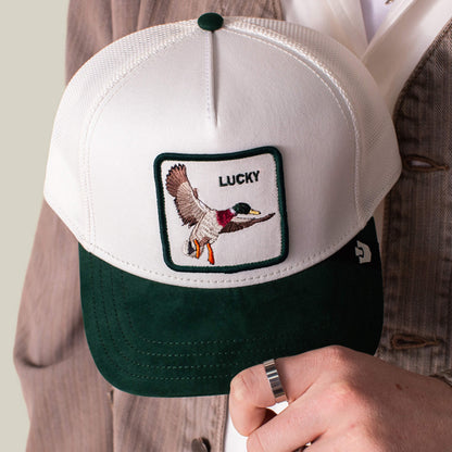 A person holds the Goorin Bros. Suede Duck cap, a green and white baseball hat with a duck patch and "LUCKY" on the crown.