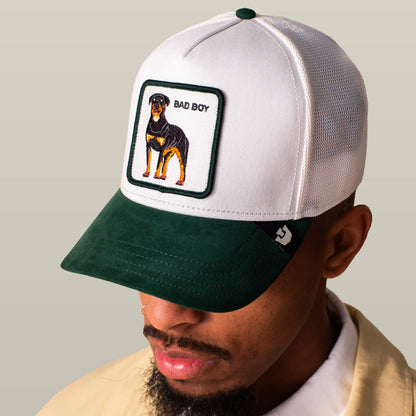 A man wears the Goorin Bros. Suede Bad Boy trucker hat, featuring a white and green design with a Rottweiler patch and BAD BOY text on the front.