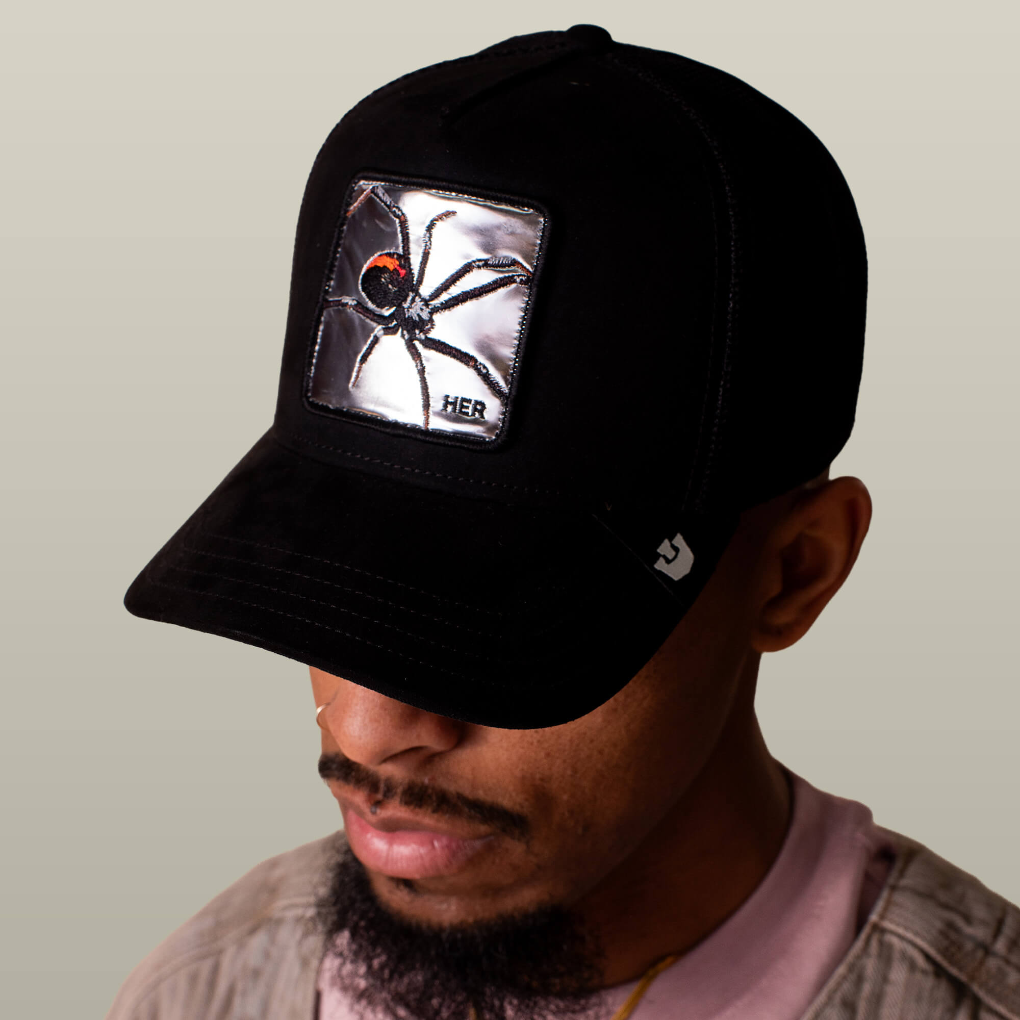 A person wears the Goorin Bros. "Silver Spider" black trucker hat with a large silver spider patch on the front, looking downward against a plain background.