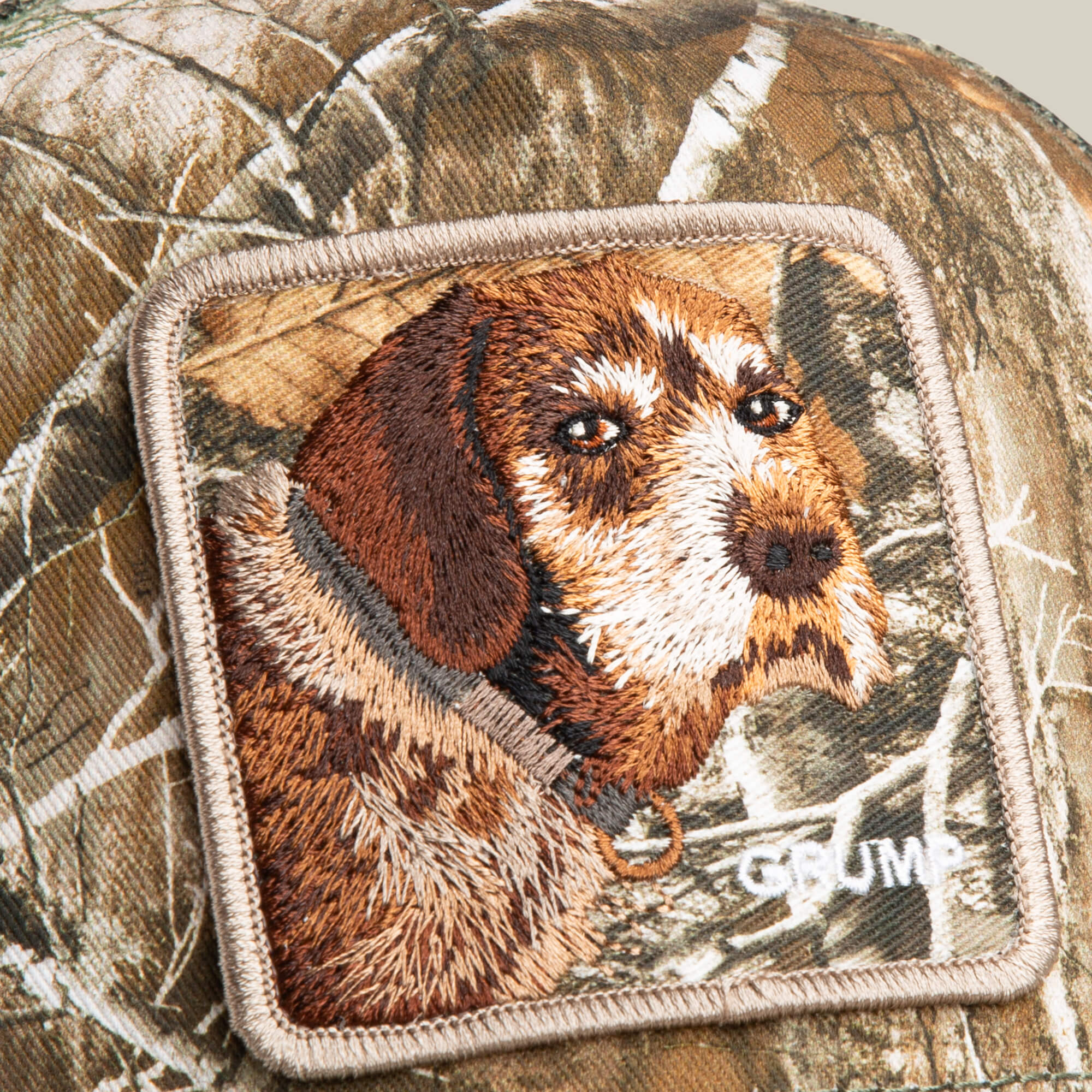 The Realtree Edge Grump Dog by Goorin Bros. features camo fabric with a sewn patch showing an embroidered brown and white dog’s face and "GRUMP" in bold white letters.