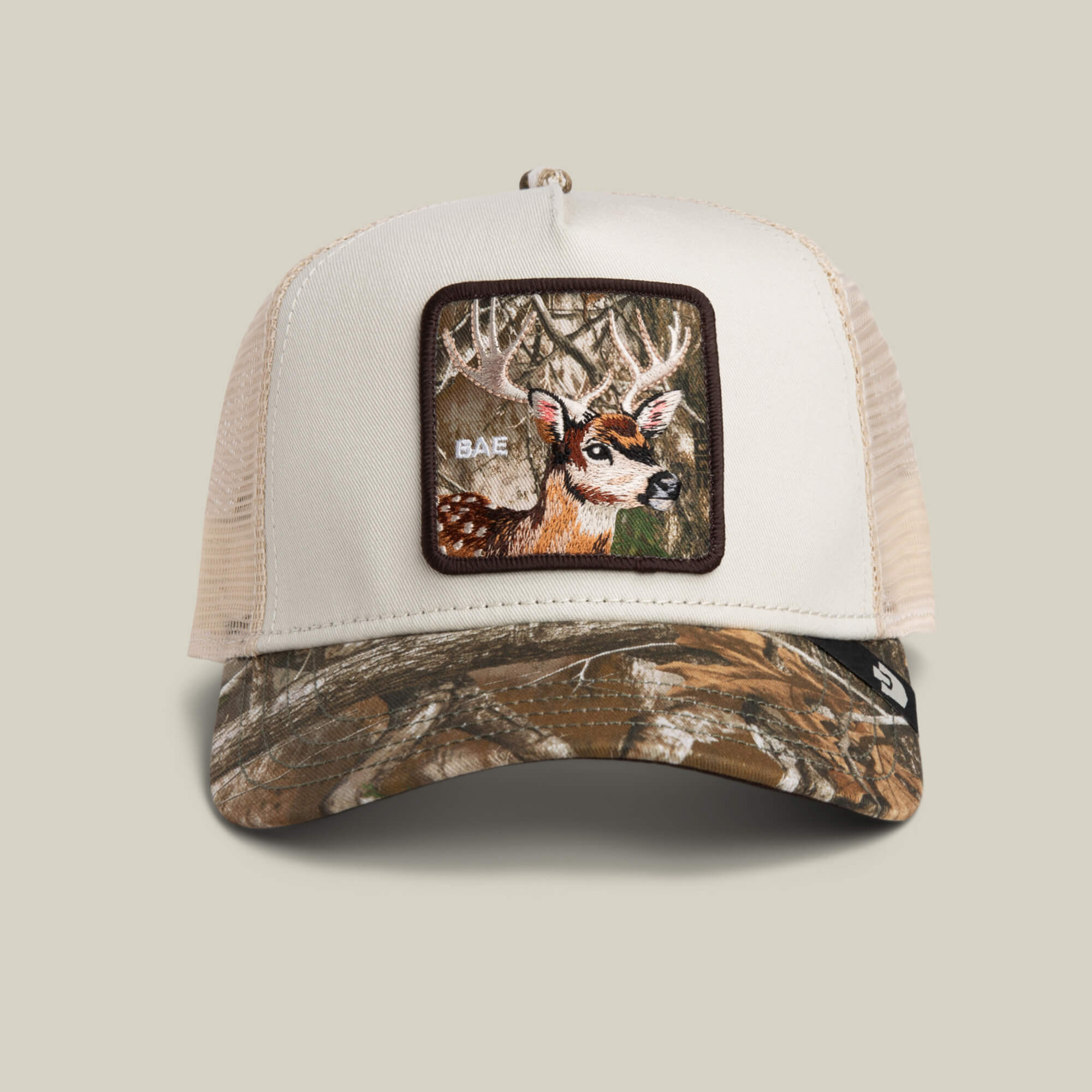 The Goorin Bros. Realtree Edge Bae Doe trucker hat features a camouflage design and an embroidered deer patch labeled “BAE” on the front panel.