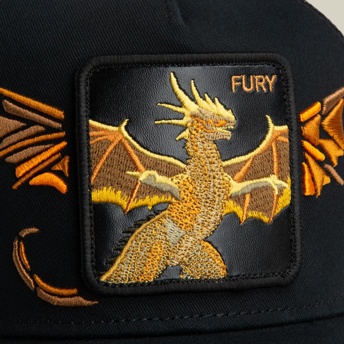 Goorin Bros. Wings Fury trucker hat featuring a gold embroidered dragon with spread wings on a black fabric patch, displayed as a close-up product shot.