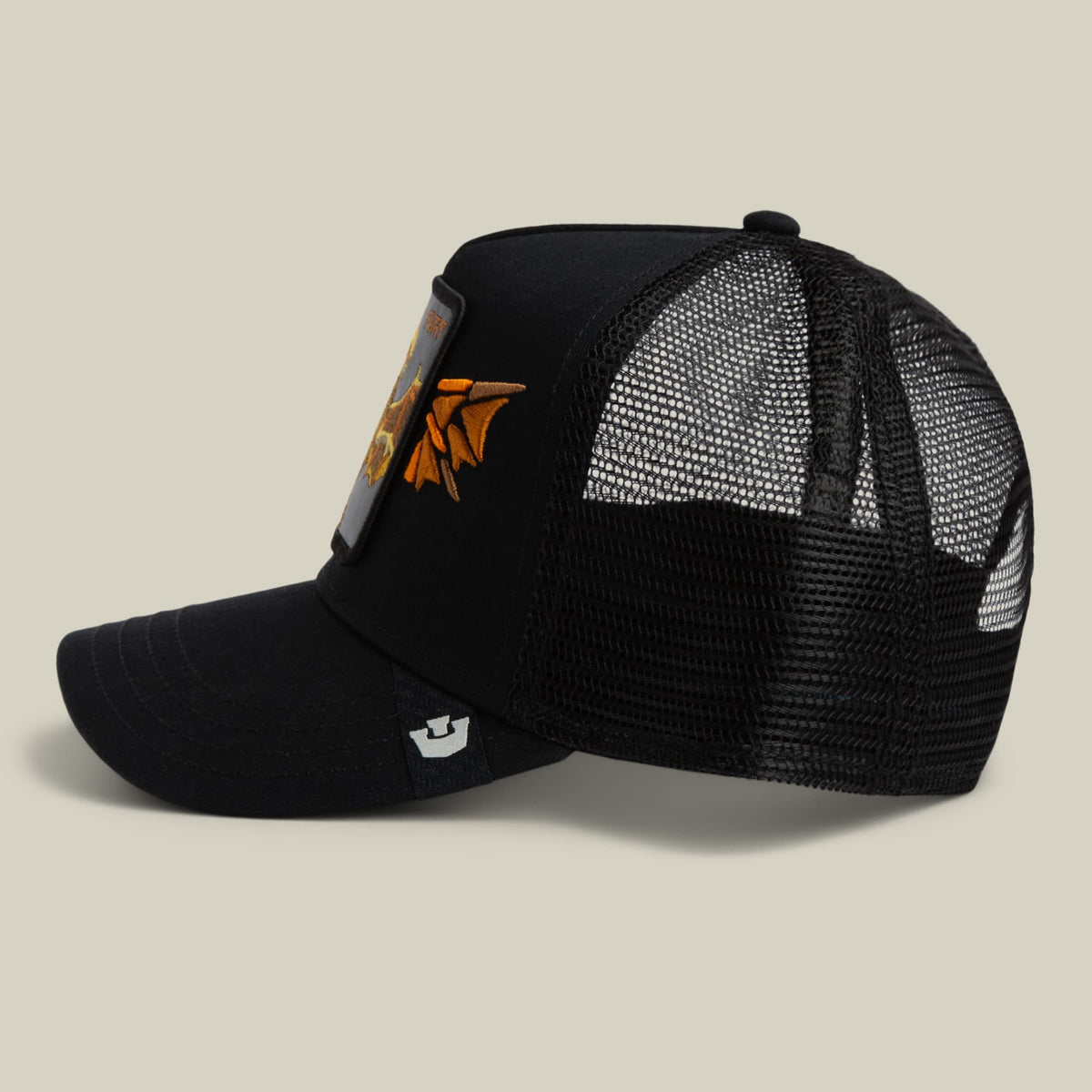 The Goorin Bros. Wings Fury black trucker hat features a mesh back, orange embroidered wings patch on the front, and an adjustable closure, displayed against a neutral beige background.