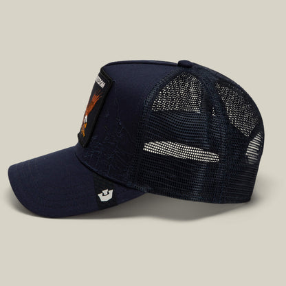 The Goorin Bros. Badlands Eagle is a navy blue trucker hat with a curved brim, side and back mesh panels, and a rectangular patch featuring an eagle on the front. The hat is displayed in profile against a plain background.