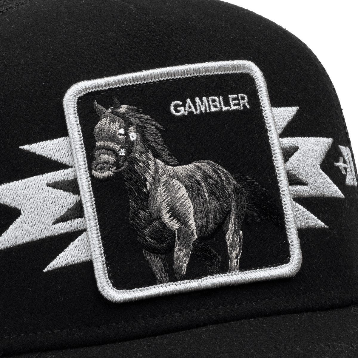 The Goorin Bros. Canyon Gambler is a black trucker hat with a white embroidered patch featuring a detailed horse graphic and "GAMBLER" text, shown in a studio close-up shot.