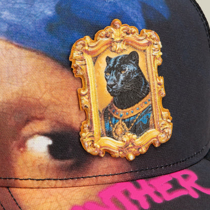 The Girl with the Pearl Necklace by Goorin Bros is a black trucker hat featuring an ornate gold-framed embroidered patch of a panther wearing a blue jeweled collar, set against a colorful gradient background with pink text at the brim.