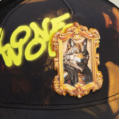 The Coming of Saint Matthew trucker hat by Goorin Bros features a black crown with neon yellow text, ornate gold-framed wolf embroidery, and mesh back panel in a close-up product shot.