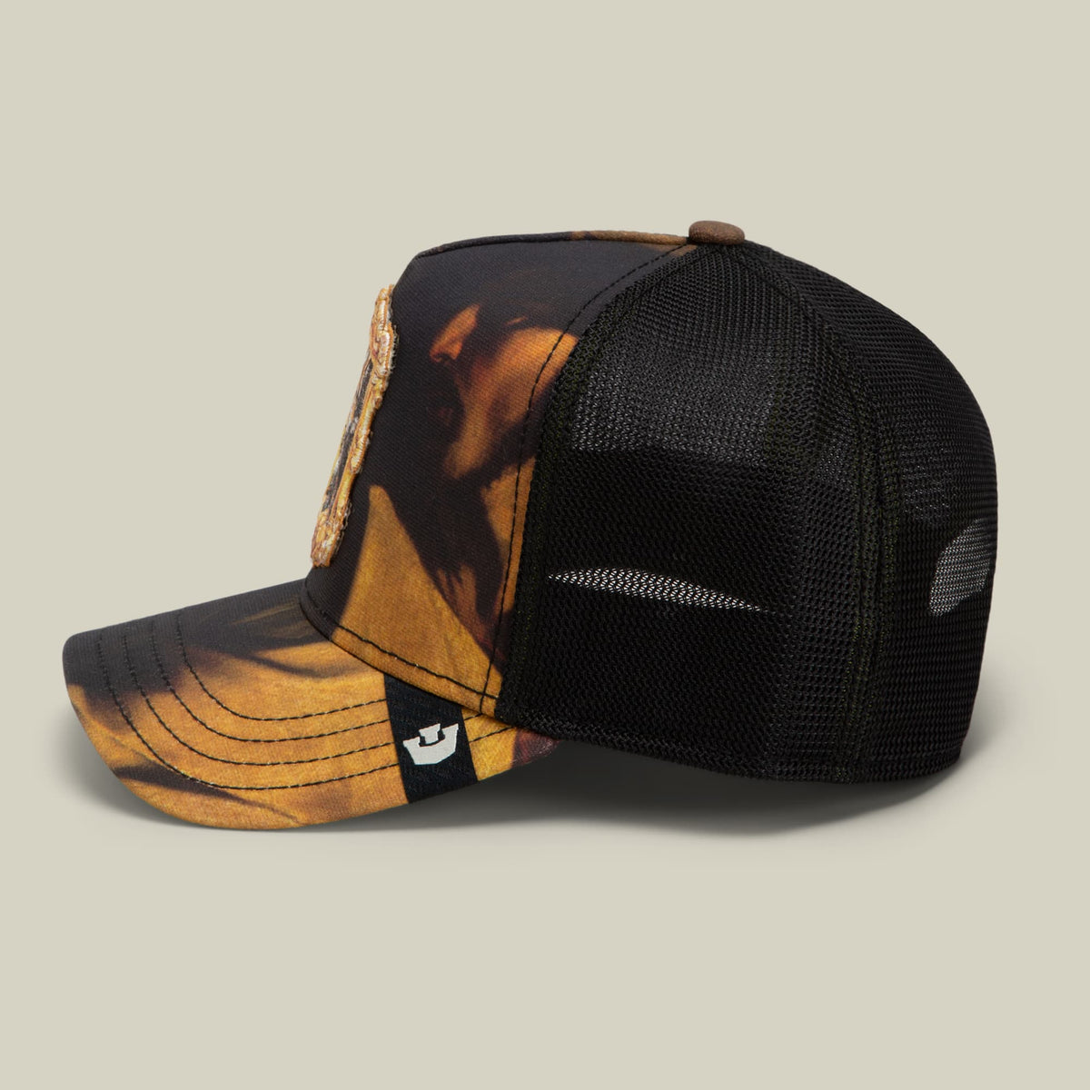 The Coming of Saint Matthew trucker hat by Goorin Bros features a black mesh back panel with an orange and gold animal print front panel, displayed in a studio side view against a neutral background.