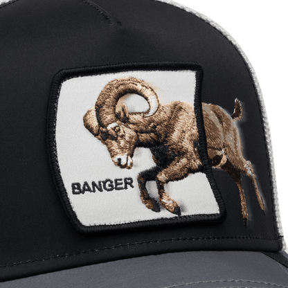 The Goorin Bros. Migration Banger trucker hat features a black and gray colorway with an embroidered patch of a brown goat on the front panel.