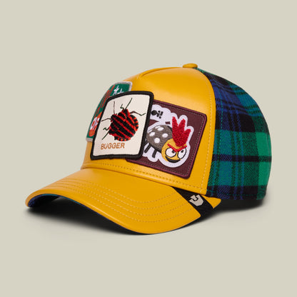 The Goorin Bros. Bugger yellow trucker hat features embroidered patches with a red ladybug and rooster design, green and navy plaid fabric on the back panels, and navy blue trim.