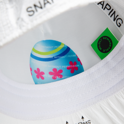 A close-up of the inside of the limited edition K.I.S.S. white hat by Goorin Bros. shows a colorful egg with pink flowers, blue stripes, a green label, and black printed text.