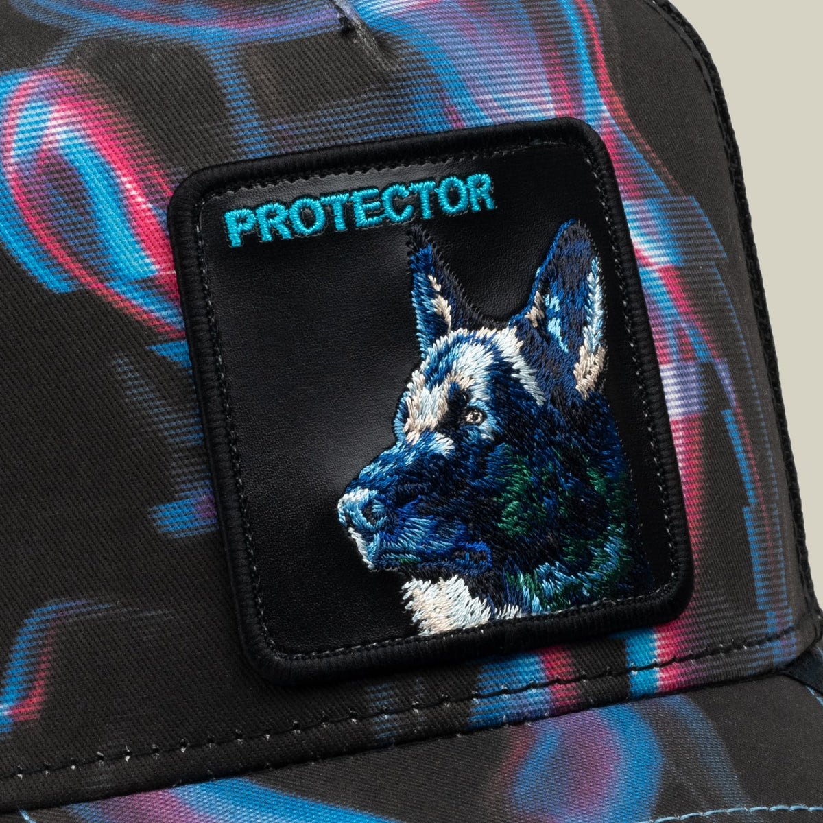 The Goorin Bros. Baba Yaga trucker hat features a colorful blue and pink patterned fabric with an embroidered black patch depicting a German Shepherd's head and "PROTECTOR" text.