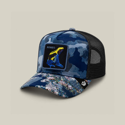 The Goorin Bros. Warfare Art Thou cap is a blue camo trucker hat with a mesh back, featuring a vibrant Romeo poison dart frog patch and the word ROMEO for playful style.