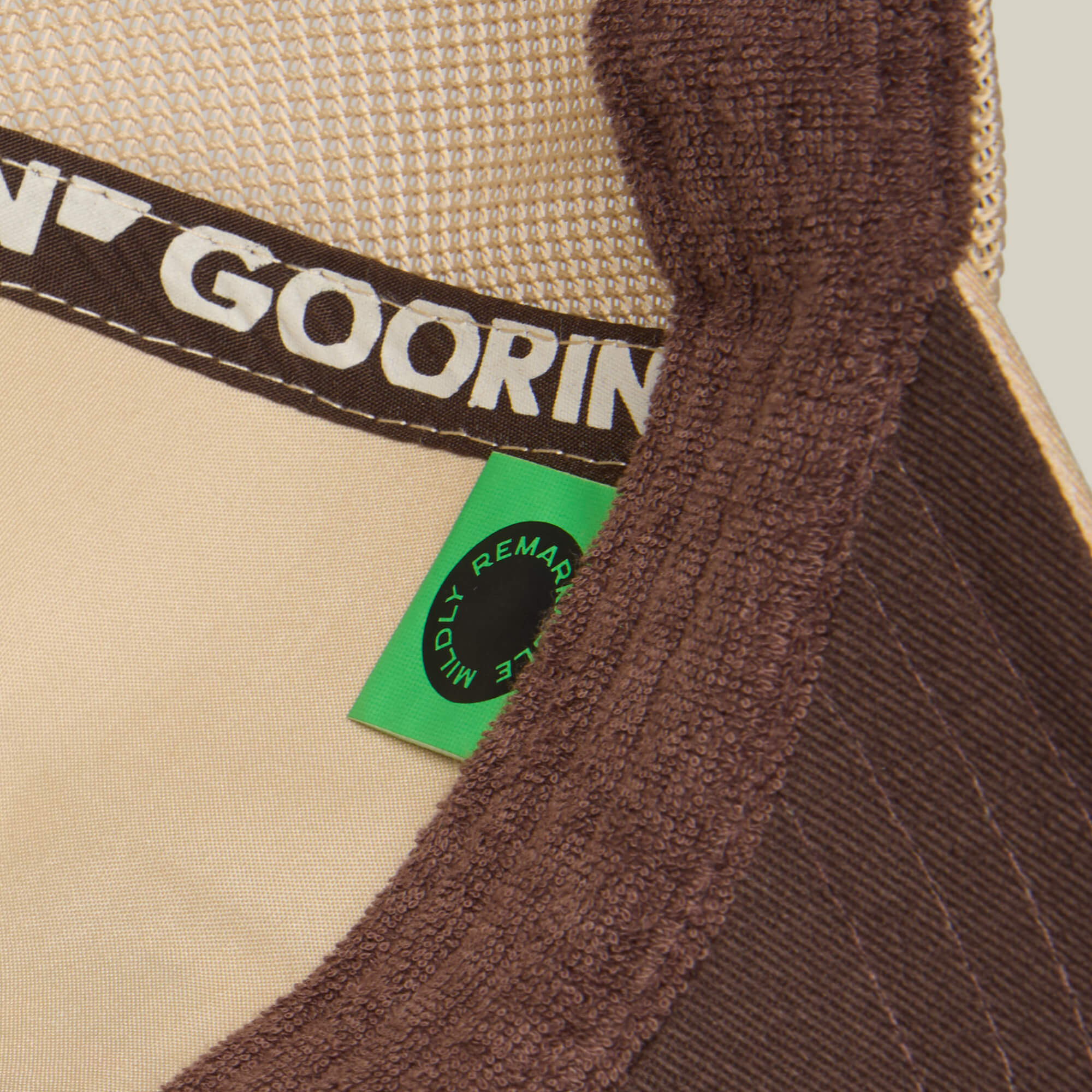 Close-up of the inside of a brown and beige Goorin Bros. "Hey, I Like It! Picasso!" hat, showing a green label with "REMARKABLY" and part of the brand name on the inner band, featuring digital print embroidery details.