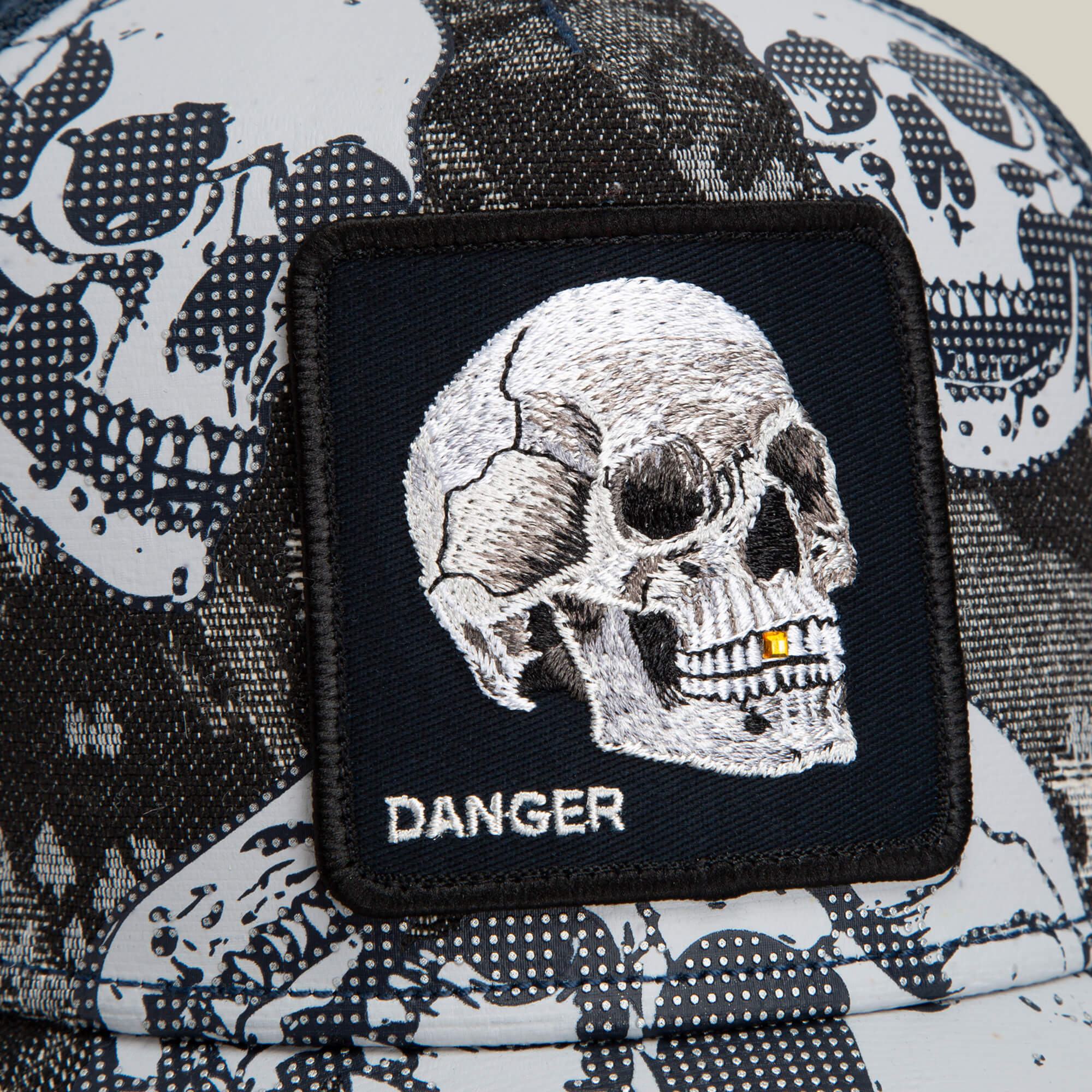 Close-up of the Goorin Bros. Bone Head Danger trucker cap, featuring a black and white mesh-back design with a patch displaying an embroidered skull and the word “DANGER” beneath it.