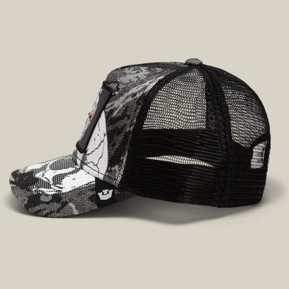 The Goorin Bros. Bone Head Unalive is a black and white mesh trucker hat with an abstract pattern, featuring a rectangular patch on the front and an adjustable snapback closure for a customizable fit. Designed for comfort, its breathable mesh back is highlighted as the hat is displayed from the side against a beige background.