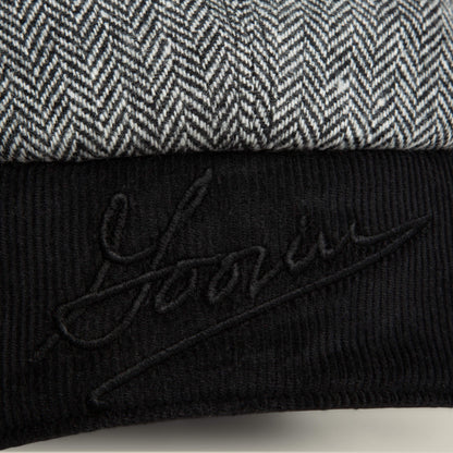 A close-up of the Goorin Bros. Frazier Lake hat, showing gray and white herringbone fabric with ear flaps and a black corduroy section embroidered with "Yours.