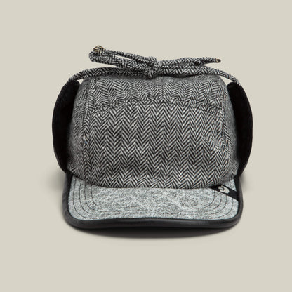 The Goorin Bros. Frazier Lake trapper hat in OIL features herringbone wool, fold-down ear flaps, a short brim, and a tied string on top, shown facing forward on a plain background.
