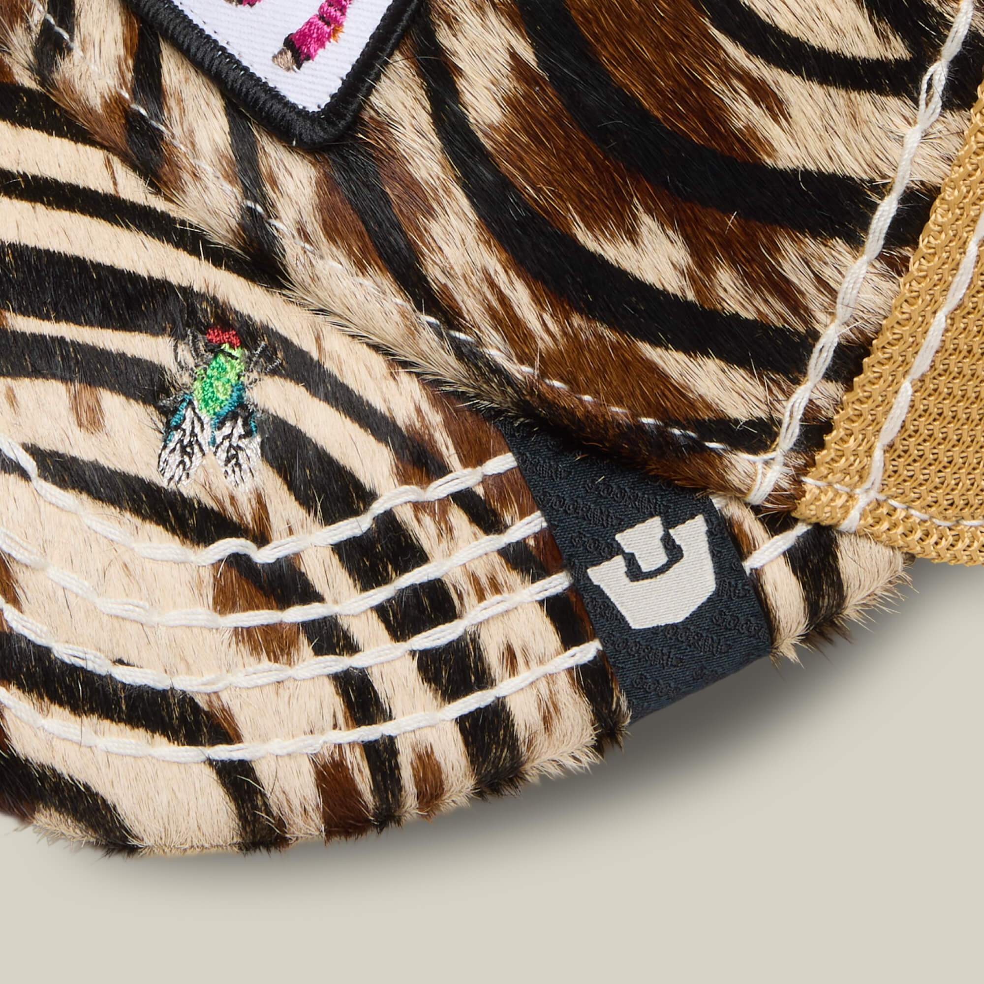 A close-up of the Goorin Bros. Tijuana Special hat featuring faux fur with tiger stripes, yellow mesh, a small embroidered fly, and a black tag with a white logo.