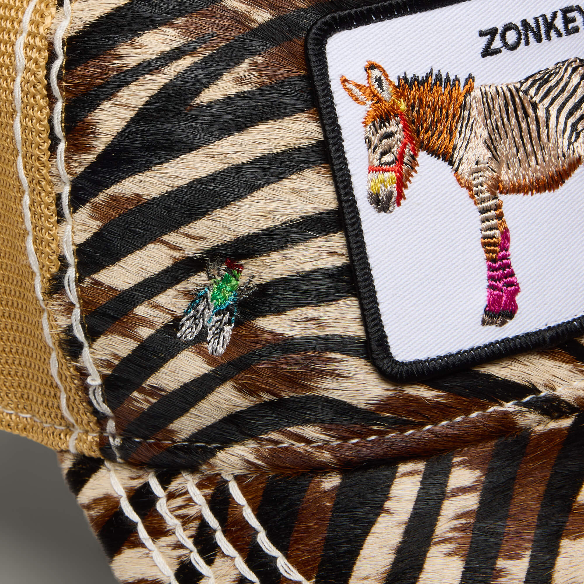 A close-up of the Goorin Bros. Tijuana Special shows its zebra-patterned design, zebra patch labeled "Zonkey," and an embroidered fly—features inspired by Africa.