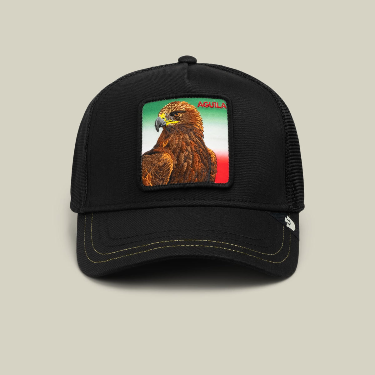The Metallic Gradient Aguila by Goorin Bros is a black trucker hat featuring an embroidered eagle patch with Mexican flag colors on the front and mesh back panels.