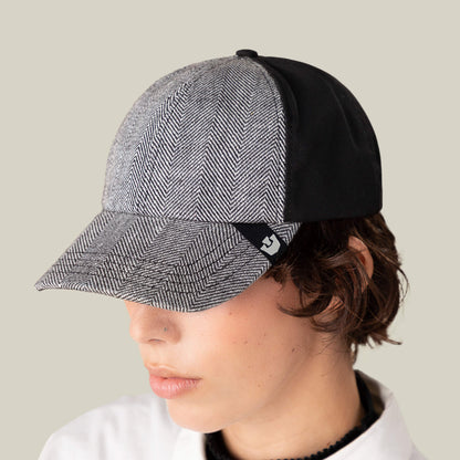 Someone wearing the Goorin Bros. Zig Zag Tailored Baseball hat in gray herringbone with black back panels, looking downward against a plain beige background.