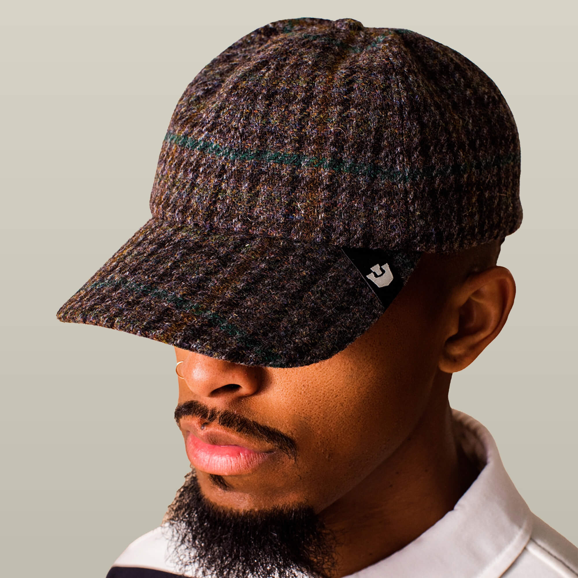 A man wears the Goorin Bros. Cozy Tailored Baseball cap—a plaid design in muted tones with a black logo tag—while facing slightly downward against a beige background.