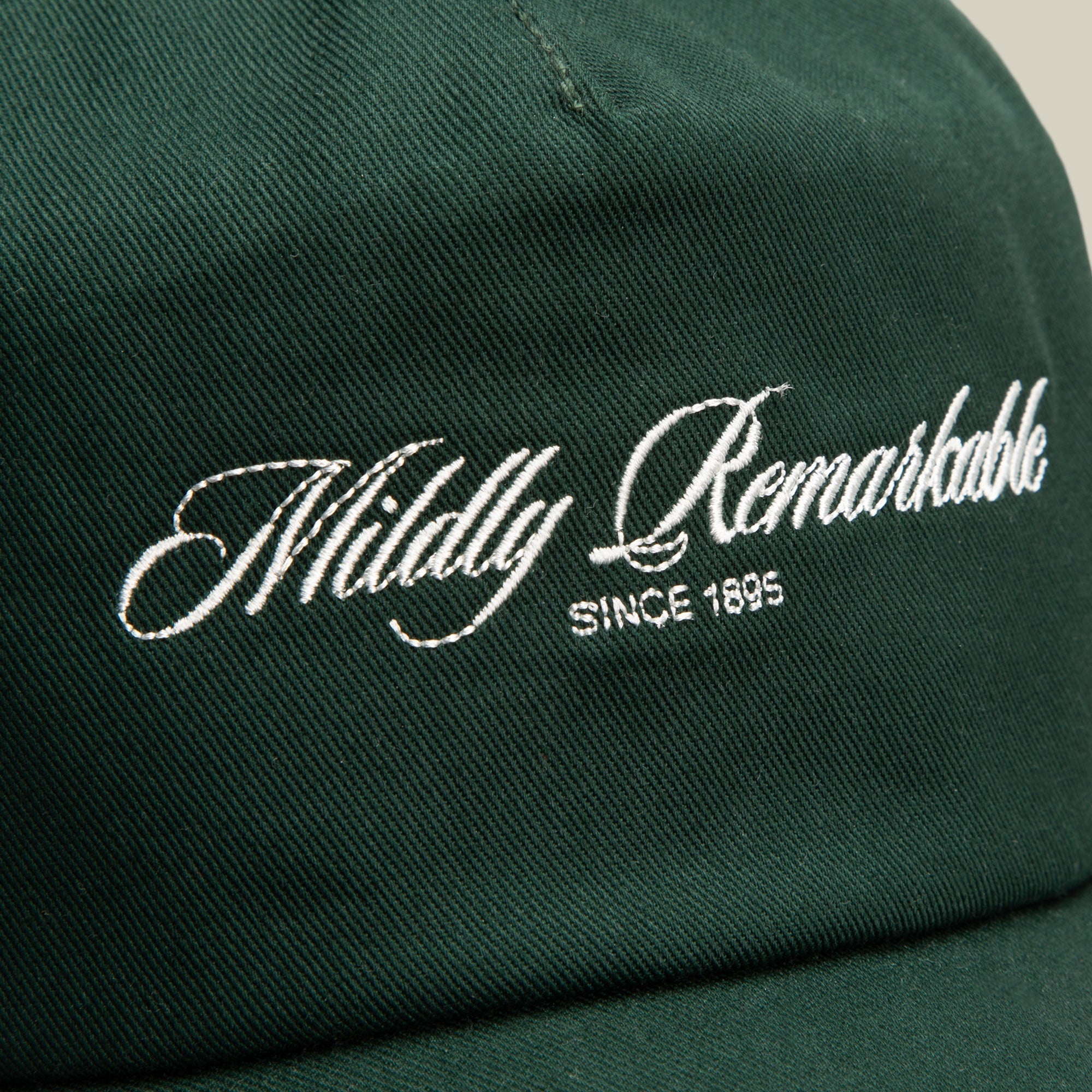 Close-up of the Goorin Bros. Mildly Remarkable Script dark green low pro fit cap featuring "Mildly Remarkable" and "SINCE 1895" embroidered in white script on the front, highlighting its classic embroidery.