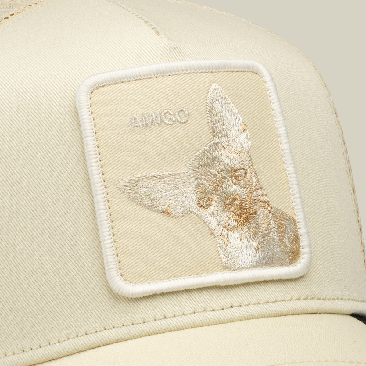 The Goorin Bros. Tonal Amigo cream trucker hat features an embroidered animal patch on the front panel against a neutral beige background in a close-up studio shot.