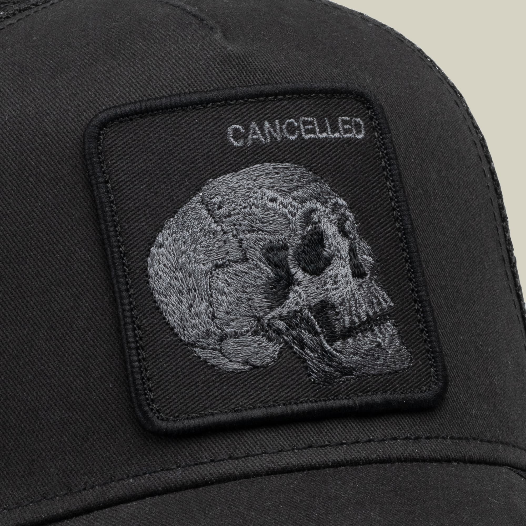 The Goorin Bros. Tonal Skull black trucker hat features an embroidered gray skull patch with "CANCELLED" text, shown in close-up detail against a neutral background.