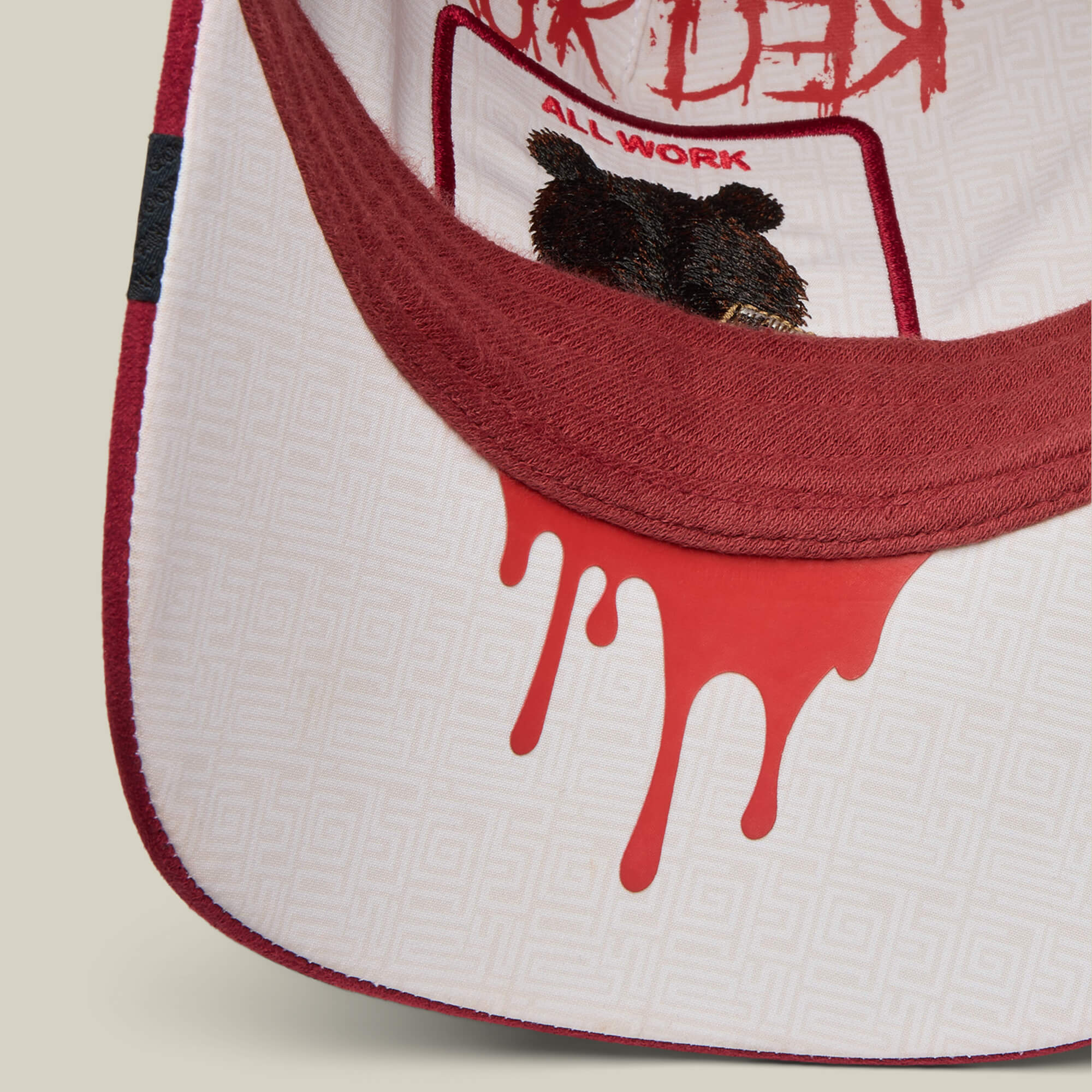 Close-up of the underside of a red and white Dull Boi hat brim by Goorin Bros., featuring a red drip design and an illustrated bear with "All Work and No Play" above—a Fresh Friday Drop inspired by Johnny.