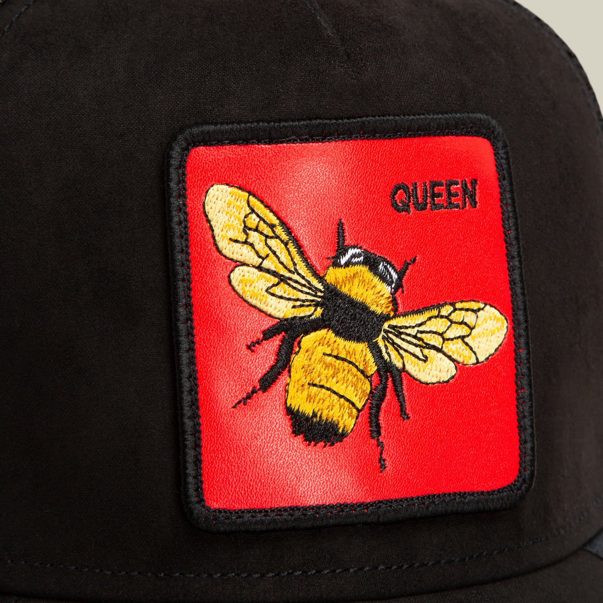The Goorin Bros. Regina Rossa black trucker hat features a red embroidered patch with a yellow and black bee design and "Queen" text on the front.