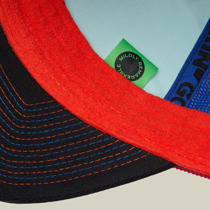 The Goorin Bros. Bug Fixes hat displayed flat lay showing red, blue, and black stitched fabric panels with a green mildly rave label against a light blue background.
