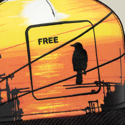 It Was The Hat trucker cap featuring a vibrant yellow-to-orange gradient sunset scene with a silhouetted bird perched on a wire and the word FREE embroidered on the crown.