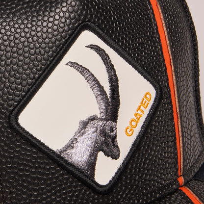 The Goorin Bros. Know Ball trucker hat features black mesh panels, a white front patch with embroidered goat design, orange text logo, and orange accent trim in a close-up product shot.