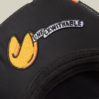 The Goorin Bros. Know Ball trucker hat features a black fabric crown with a yellow embroidered smiley face logo and white curved text on the front, shown in a close-up studio product shot.