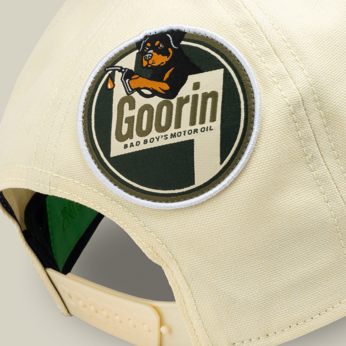 Close-up of the back of a light yellow cap by Goorin Bros., featuring a round patch with a dog holding a dropper and the text “Goorin Bad Boys Motor Oil.” The Crude Guzzler is part of the Fresh Friday drop—perfect for anyone looking for that final statement piece.