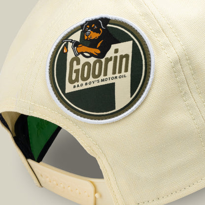 Close-up of the back of a light yellow cap by Goorin Bros., featuring a round patch with a dog holding a dropper and the text “Goorin Bad Boys Motor Oil.” The Crude Guzzler is part of the Fresh Friday drop—perfect for anyone looking for that final statement piece.