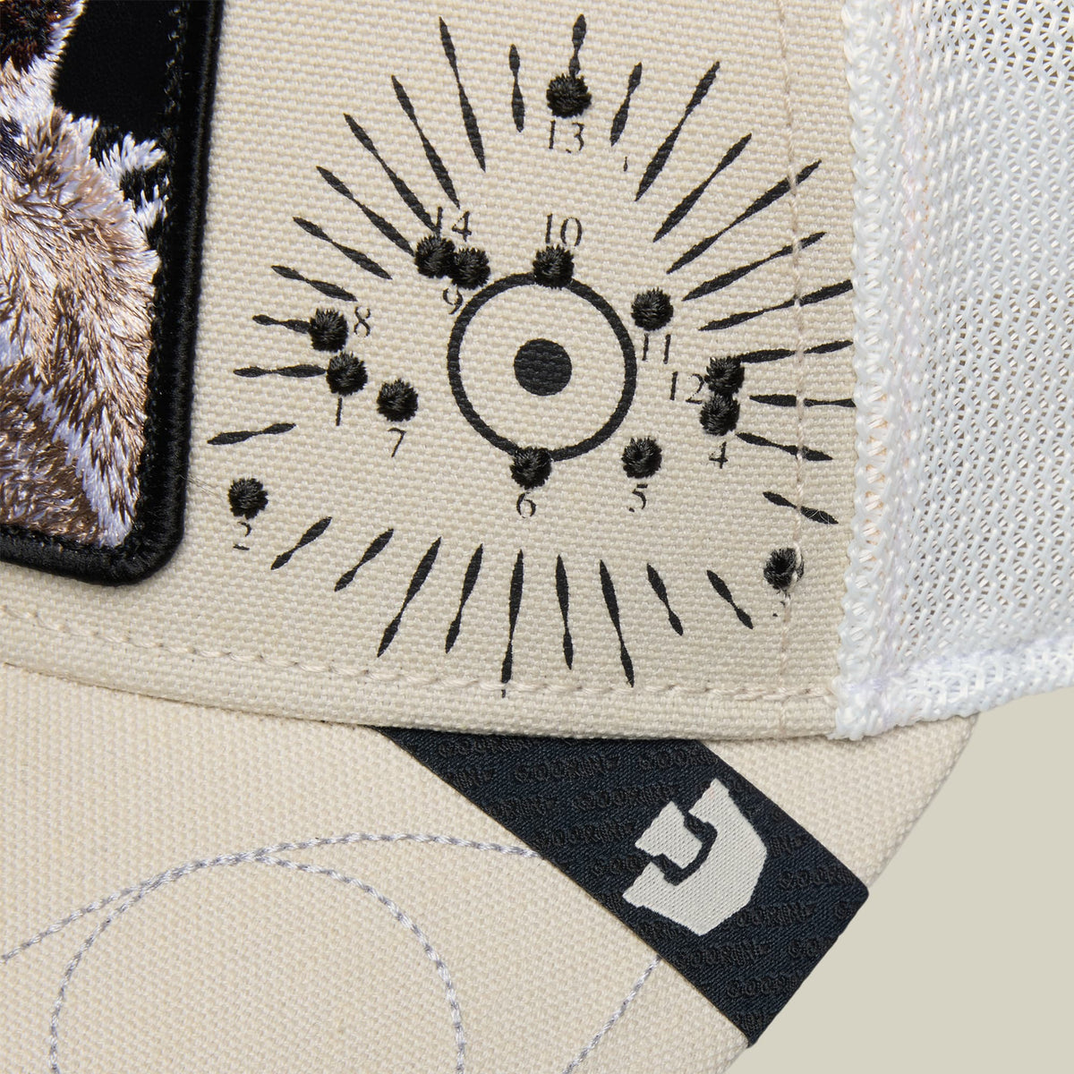 The Goorin Bros. G-Anon is a beige and cream trucker hat featuring black embroidered clock face design with numbers and radiating lines, displayed flat lay against a neutral background with brand label visible.